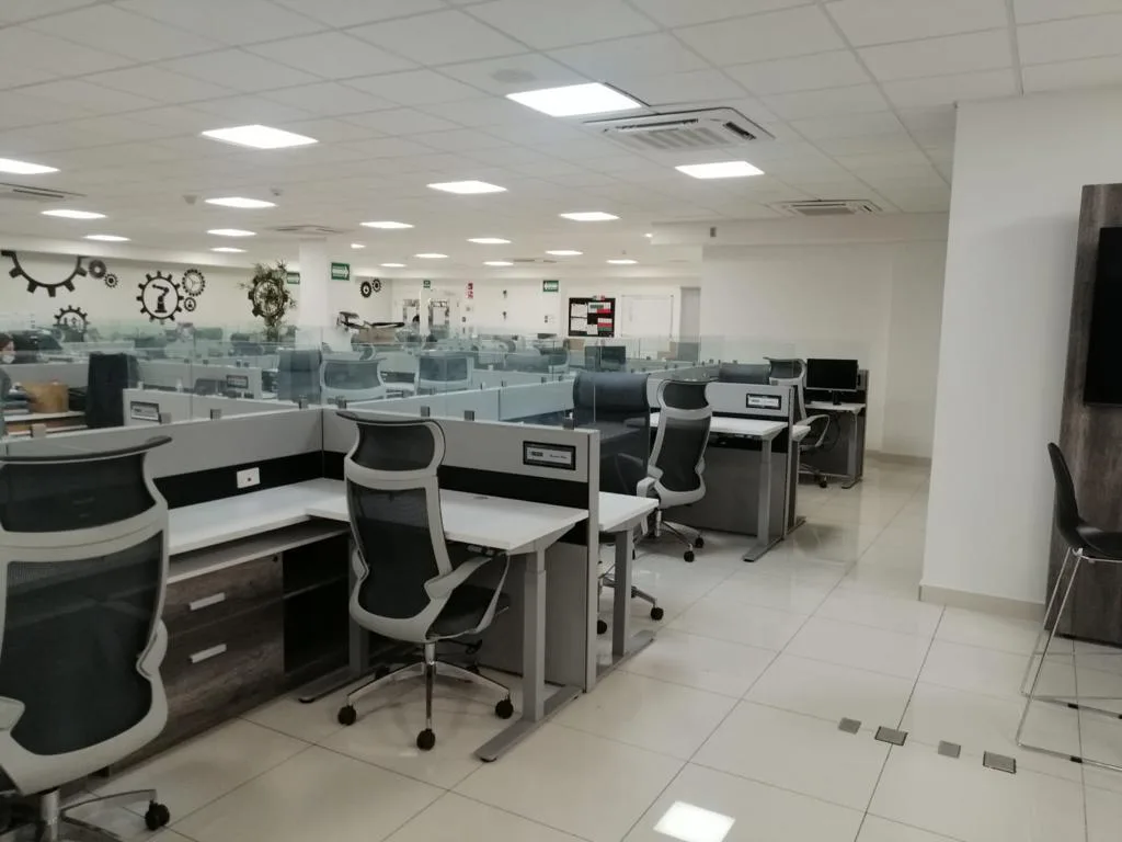 Piso de estaciones de trabajo con mamparas y sillas de malla en la planta COMPAS