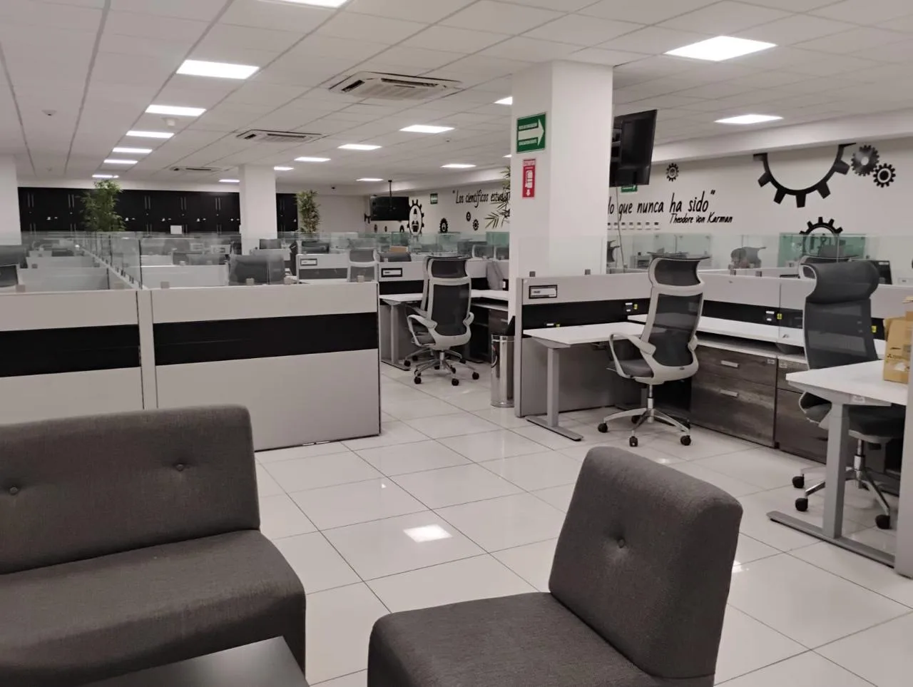 Planta abierta de oficinas con estaciones, sillas de malla y sillones de espera