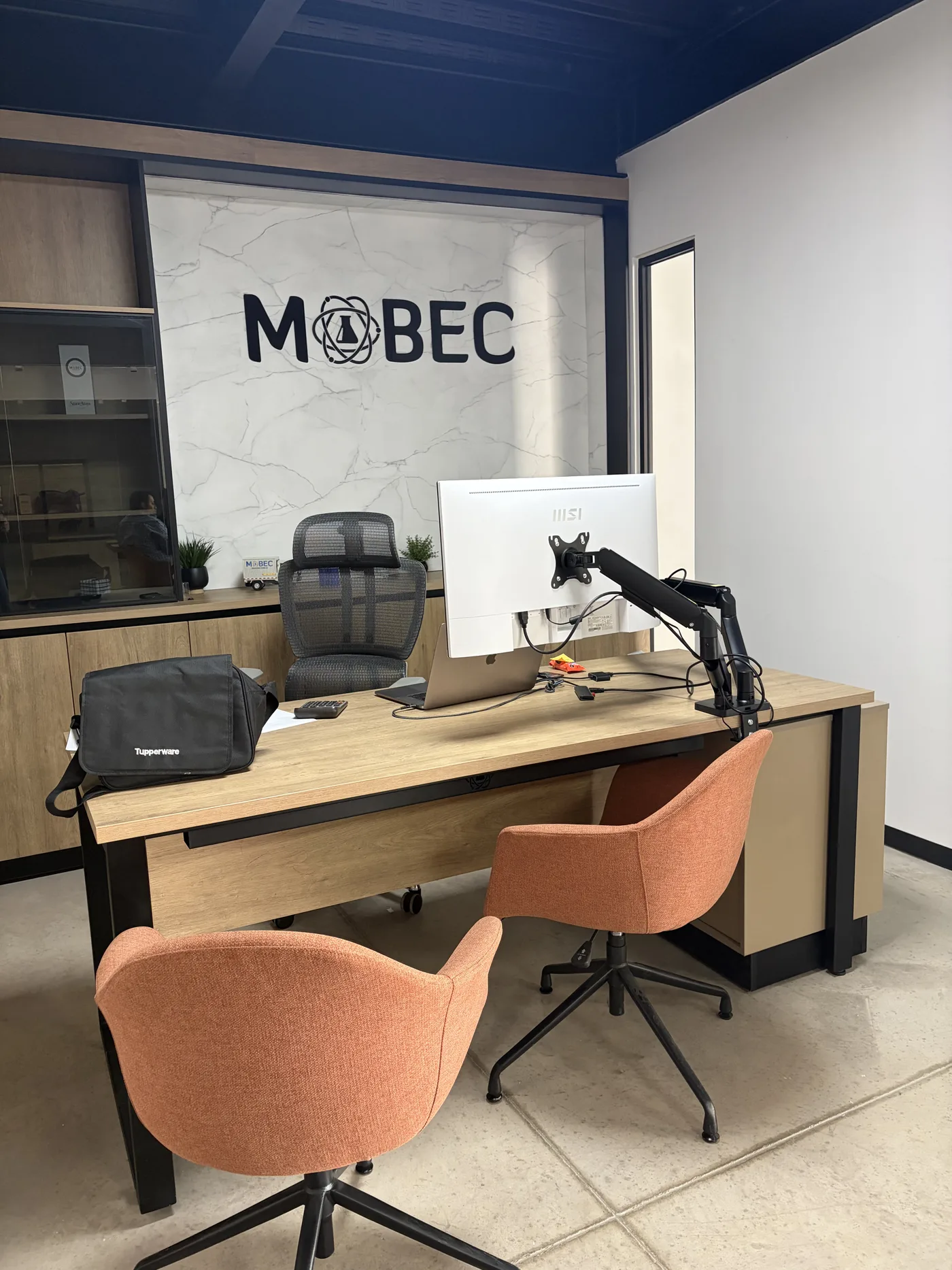 Oficina privada con escritorio de madera, sillas color terracota y muro con el logotipo del cliente